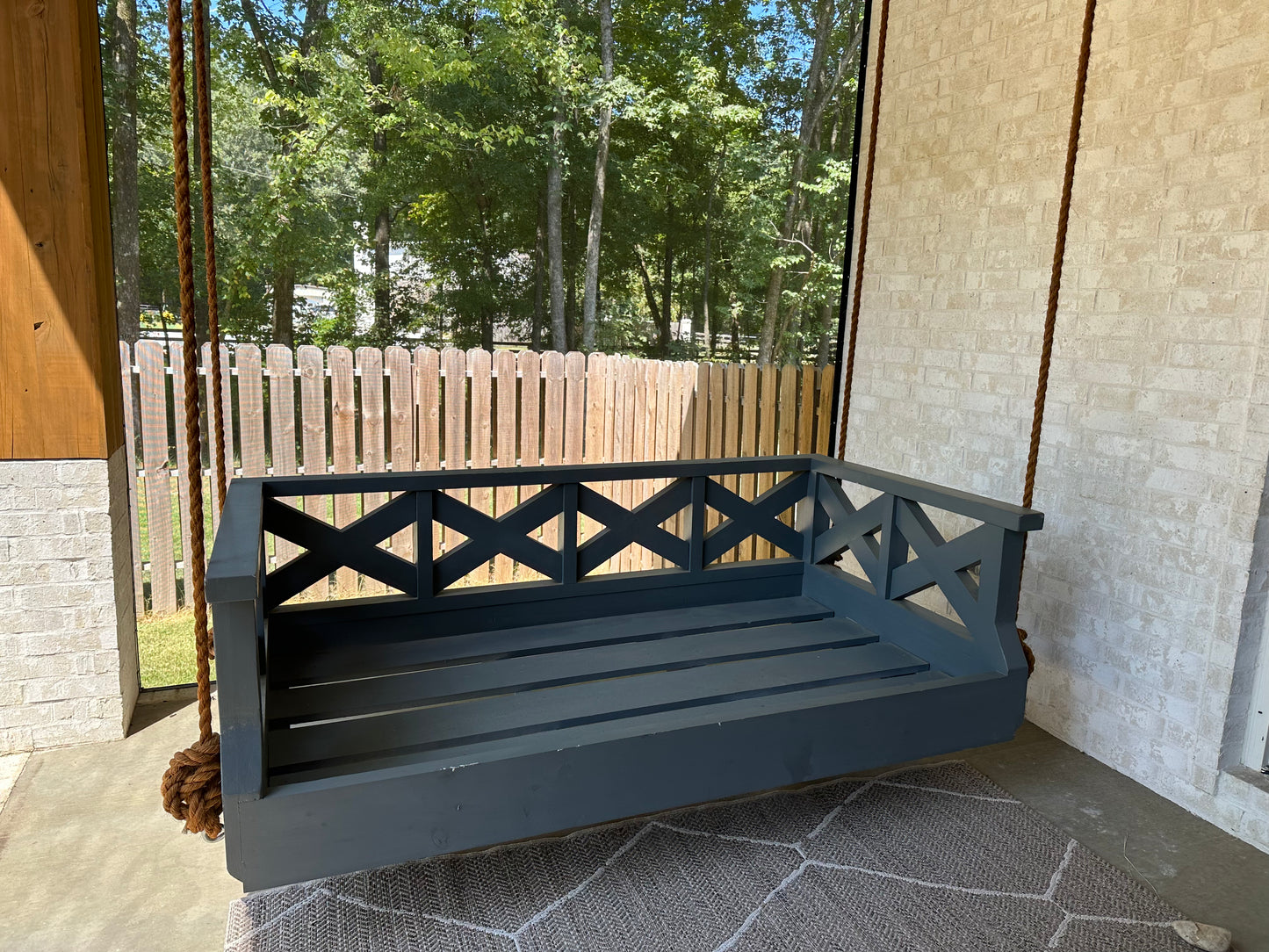 Crisscross SwingBed frame without cushions, showing the wood slat seat and crisscross side rails on a covered porch
